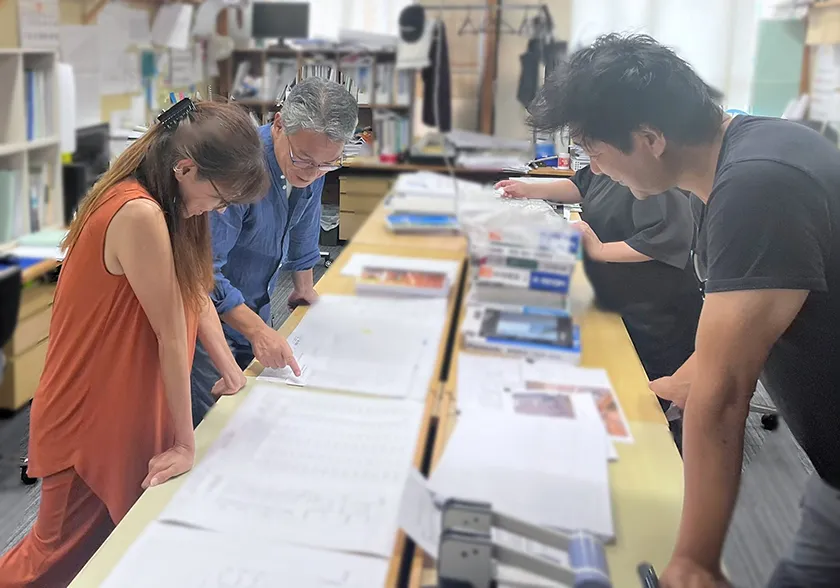 オフィスで数人がテーブルに集まり、書類を広げて議論している場面